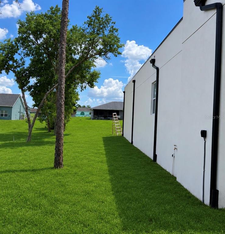 A side view of a white house exterior with black downspouts and a grassy yard — 9014 WATERBIRD WAY, BROOKSVILLE, FL