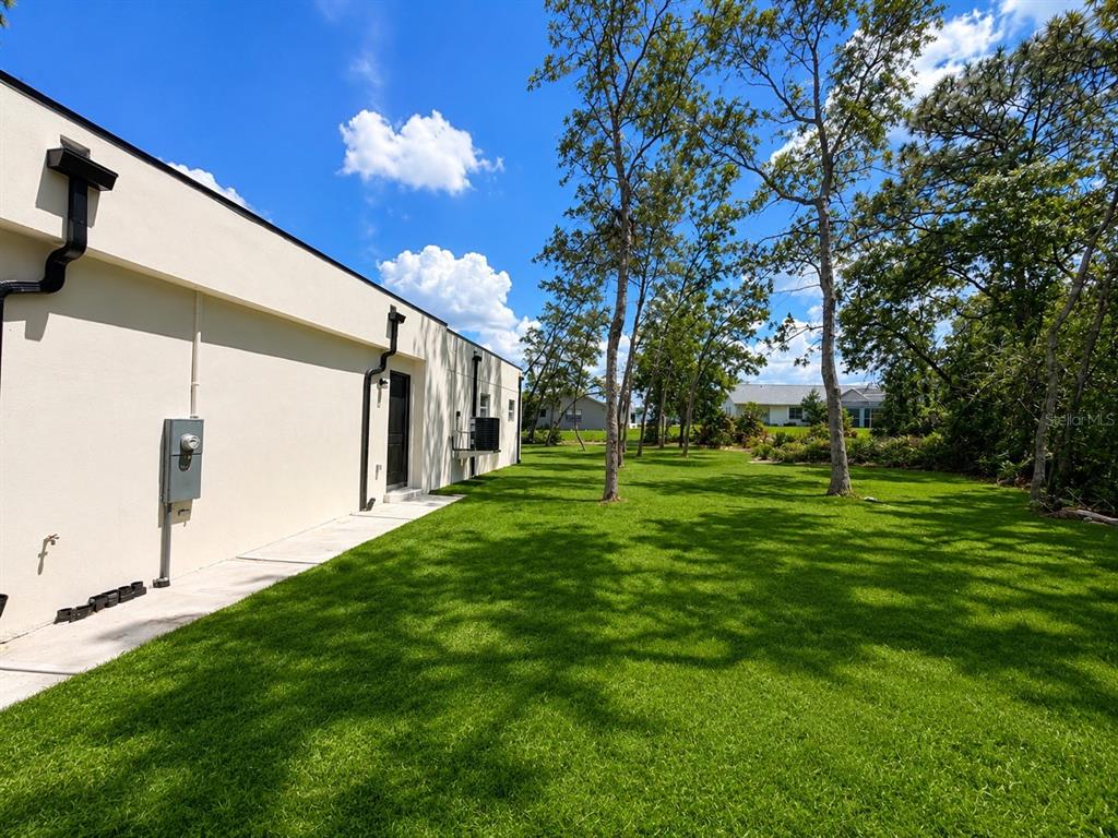 A side view of a light-colored building exterior with a grassy yard and trees — 9014 WATERBIRD WAY, BROOKSVILLE, FL