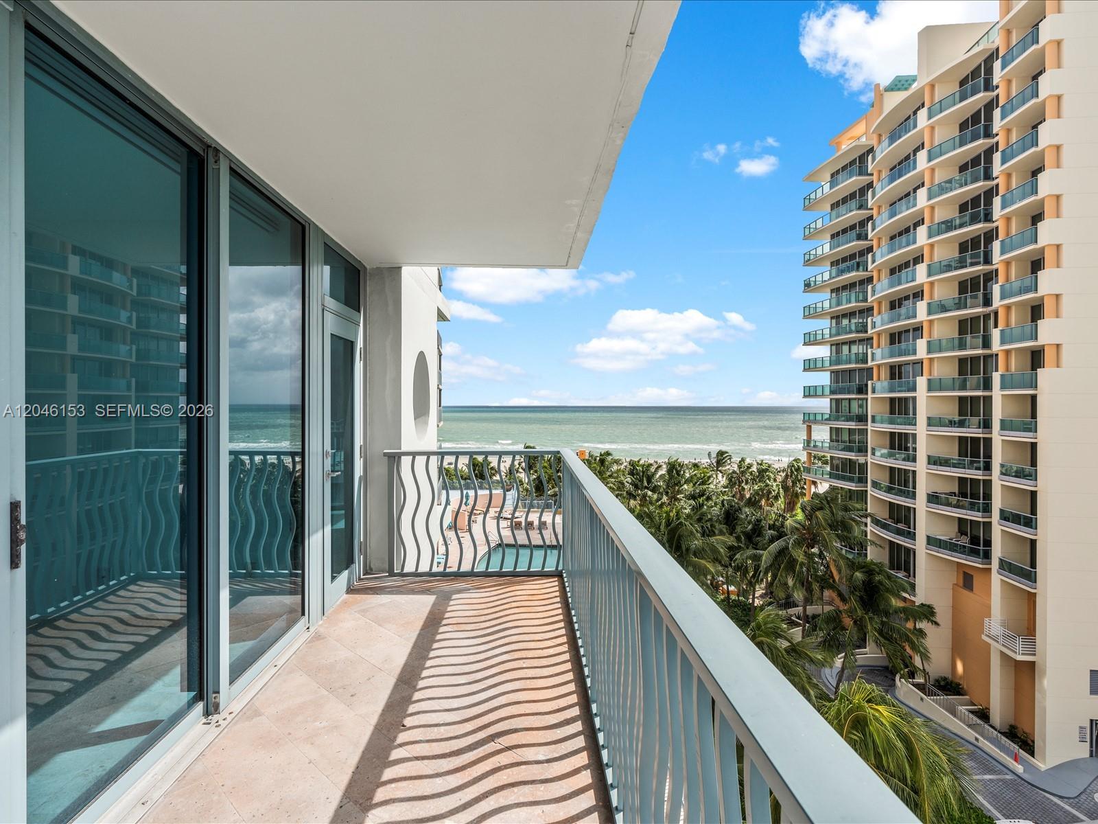 A balcony with a wavy metal railing overlooks the ocean, palm trees, and a pool — 1500 Ocean Dr # 708, Miami Beach FL 33139, MIAMI BEACH, FL