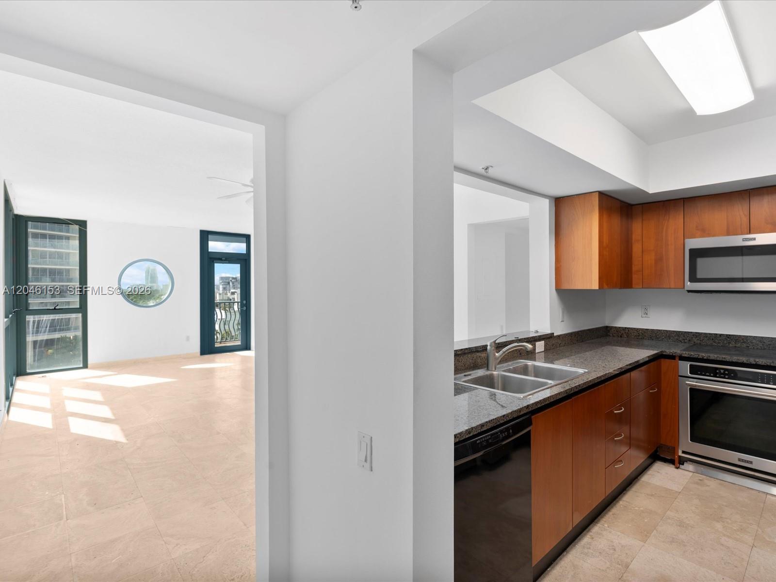 A kitchen with wood cabinets and granite countertops overlooks an adjacent living area with balcony — 1500 Ocean Dr # 708, Miami Beach FL 33139, MIAMI BEACH, FL