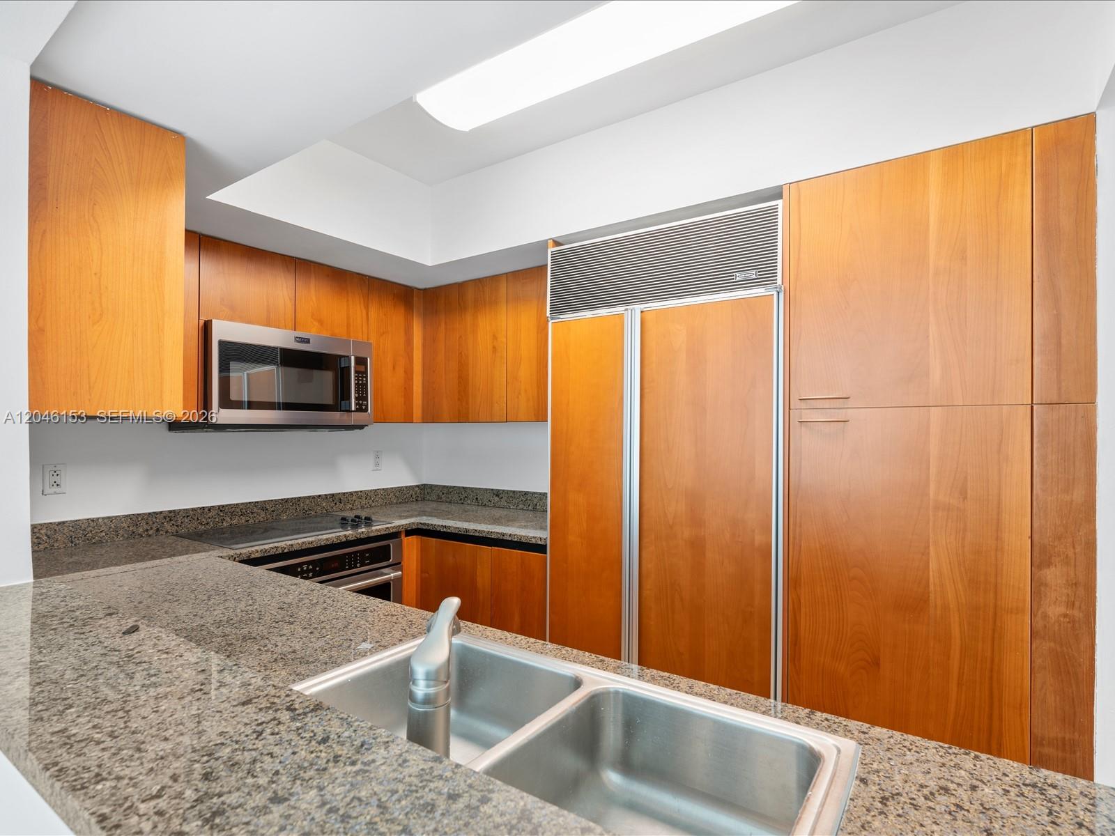 A kitchen features wood cabinetry, granite countertops, stainless steel appliances, and a double-basin sink — 1500 Ocean Dr # 708, Miami Beach FL 33139, MIAMI BEACH, FL
