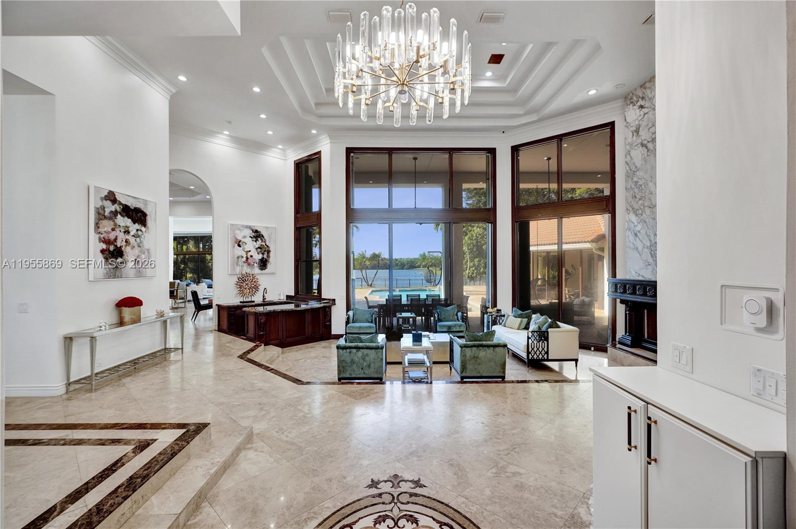 A spacious living room features a tiered tray ceiling, crystal chandelier, and large floor-to-ceiling windows — 3175 Hunter Road, Weston FL 33331, WESTON, FL