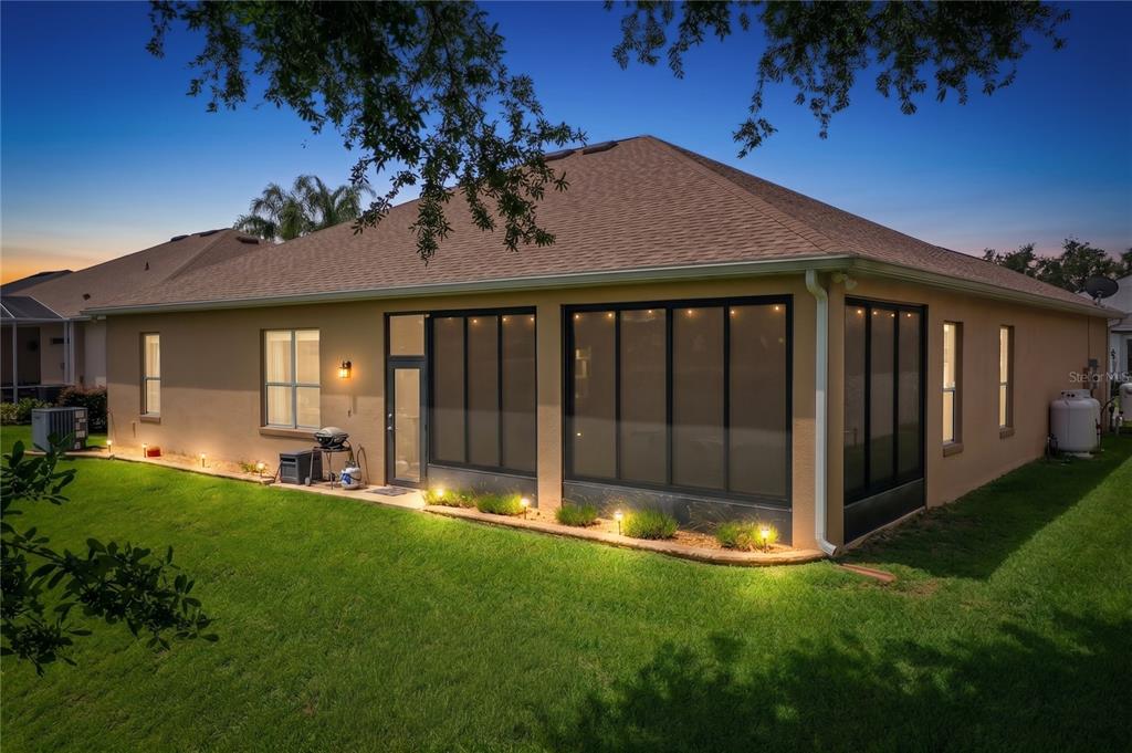 The rear exterior of a tan house features a screened-in patio and landscape lighting — 25524 LAUREL VALLEY ROAD, LEESBURG, FL