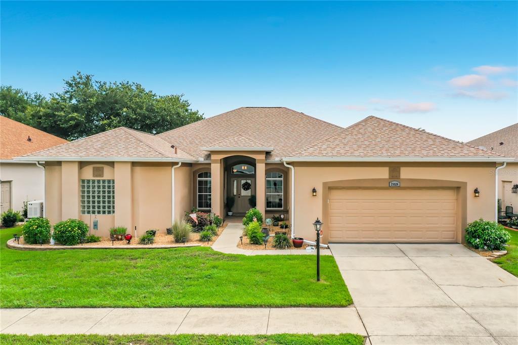 A single-story suburban house with a tan stucco exterior, a two-car garage, and a lawn — 25524 LAUREL VALLEY ROAD, LEESBURG, FL