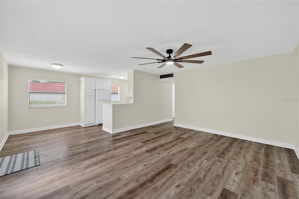 An open-concept living area features wood-look flooring, a ceiling fan, and a kitchen corner — 1802 BEDFORD LANE UNIT 12, SUN CITY CENTER, FL