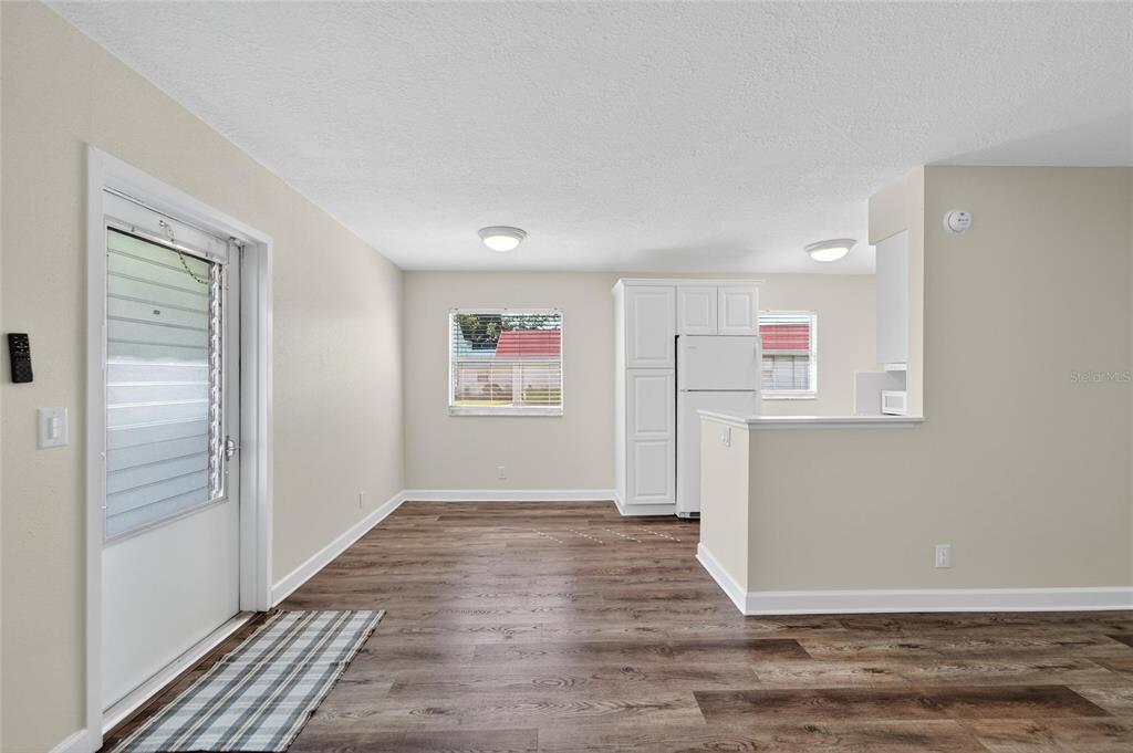 A room with wood-look flooring, a white door, a window, and a white refrigerator — 1802 BEDFORD LANE UNIT 12, SUN CITY CENTER, FL