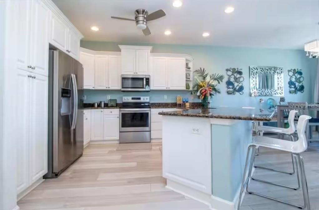 A kitchen features white cabinets, stainless steel appliances, a granite island, and light wood flooring — 2319 AVENUE C UNIT 200, BRADENTON BEACH, FL