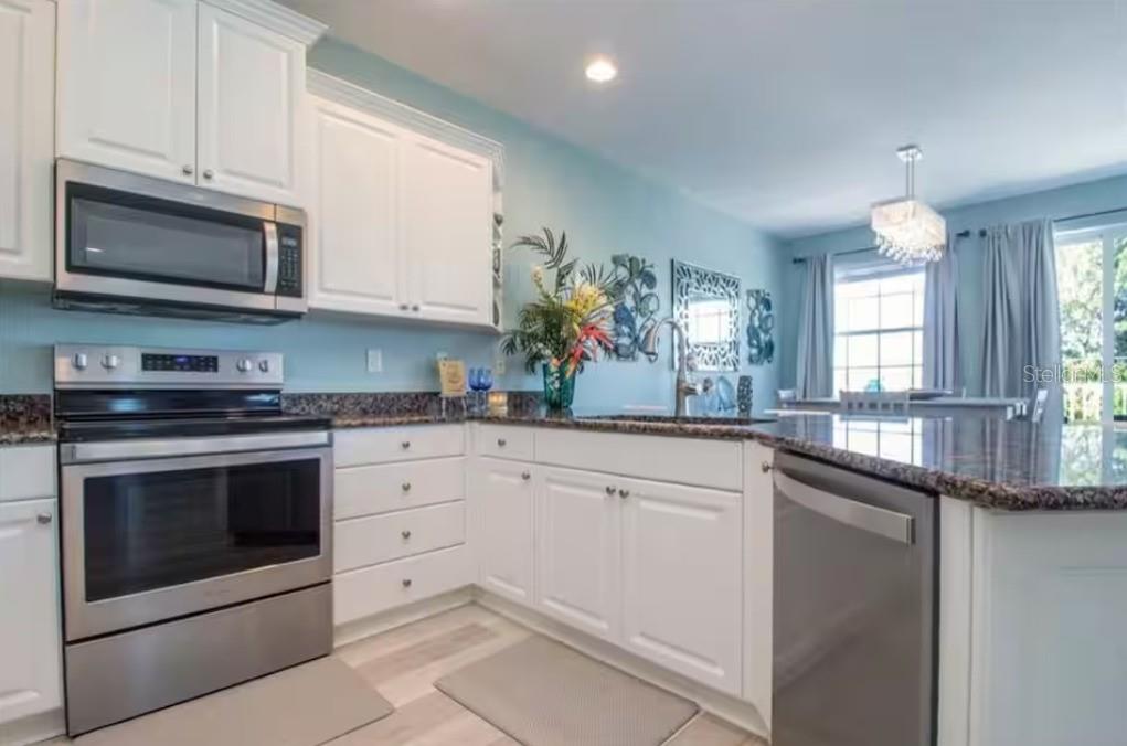 A kitchen features white cabinets, stainless steel appliances, granite countertops, and light blue walls — 2319 AVENUE C UNIT 200, BRADENTON BEACH, FL