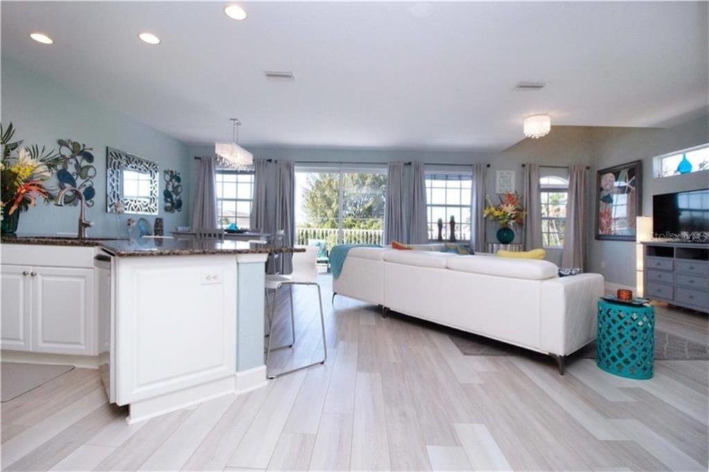 An open-concept living room and kitchen featuring white cabinetry, light wood flooring, and a sofa — 2319 AVENUE C UNIT 200, BRADENTON BEACH, FL