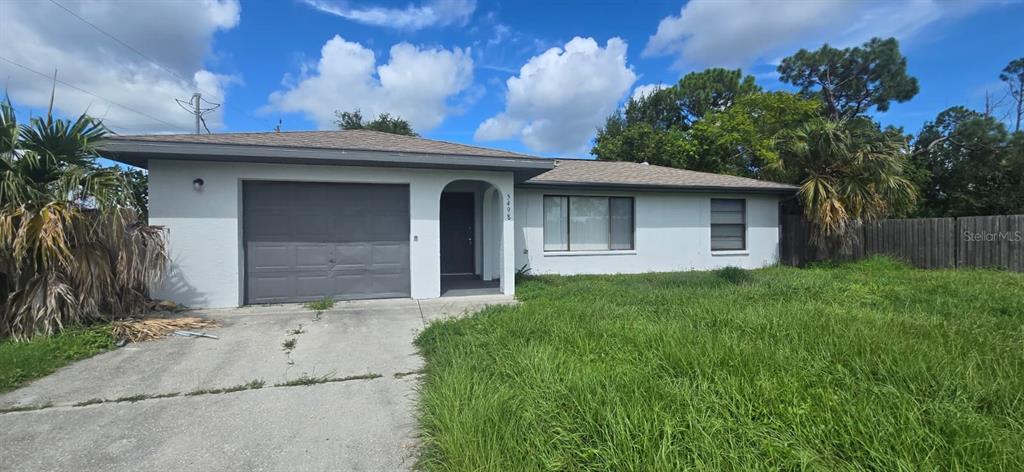 A single-story house with a gray garage door, white stucco walls, and an overgrown lawn — 5498 MONTEGO LANE, PORT CHARLOTTE, FL