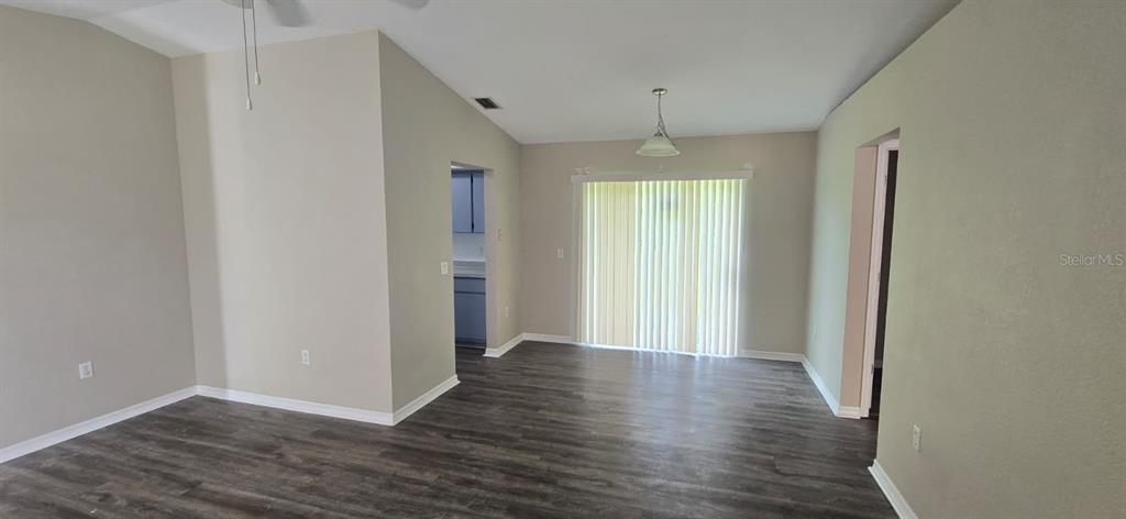 A living area with light-colored walls, dark wood-look flooring, and a sliding glass door — 5498 MONTEGO LANE, PORT CHARLOTTE, FL