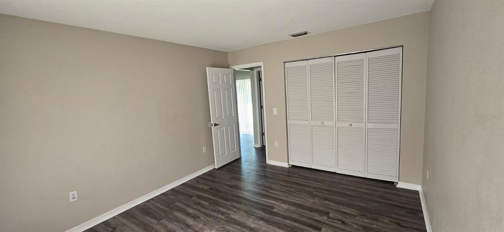 A bedroom features light-colored walls, dark wood-look flooring, and a white louvered closet door — 5498 MONTEGO LANE, PORT CHARLOTTE, FL