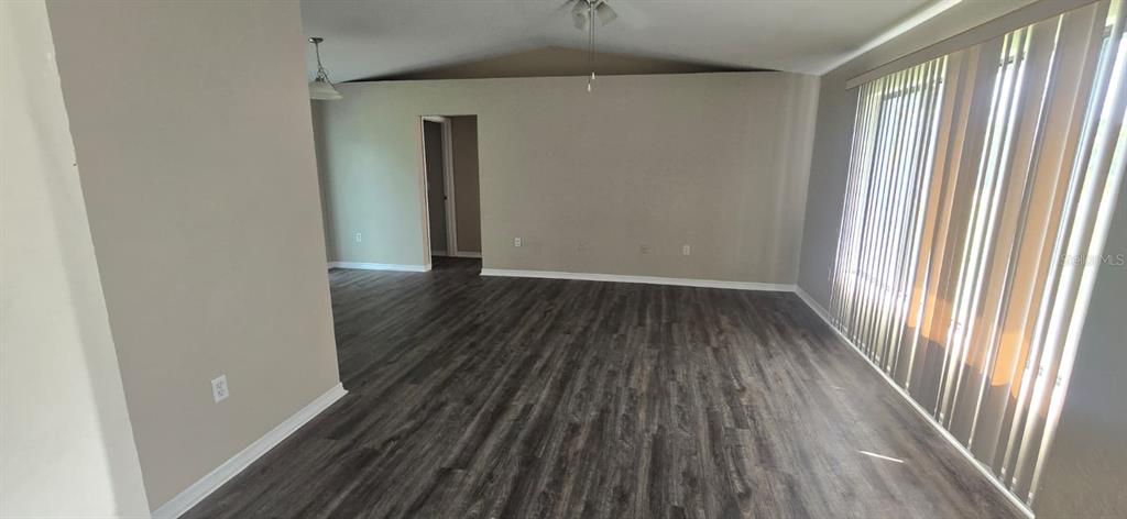 An empty room features gray walls, dark wood-look flooring, and vertical blinds on a large window — 5498 MONTEGO LANE, PORT CHARLOTTE, FL
