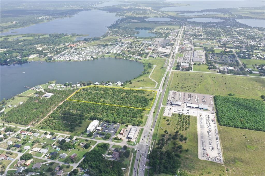 An aerial view shows a rectangular plot of undeveloped land outlined in yellow near a lake — 705 US 27 N, LAKE PLACID, FL