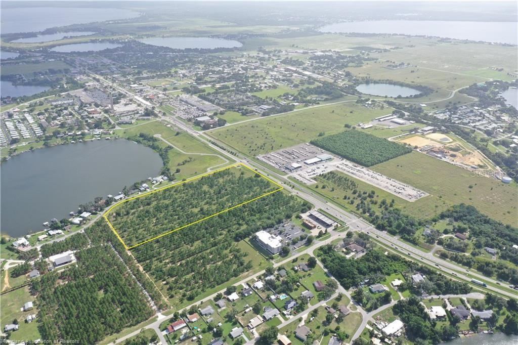 An aerial view shows a rectangular wooded lot outlined in yellow near a lake — 705 US 27 N, LAKE PLACID, FL