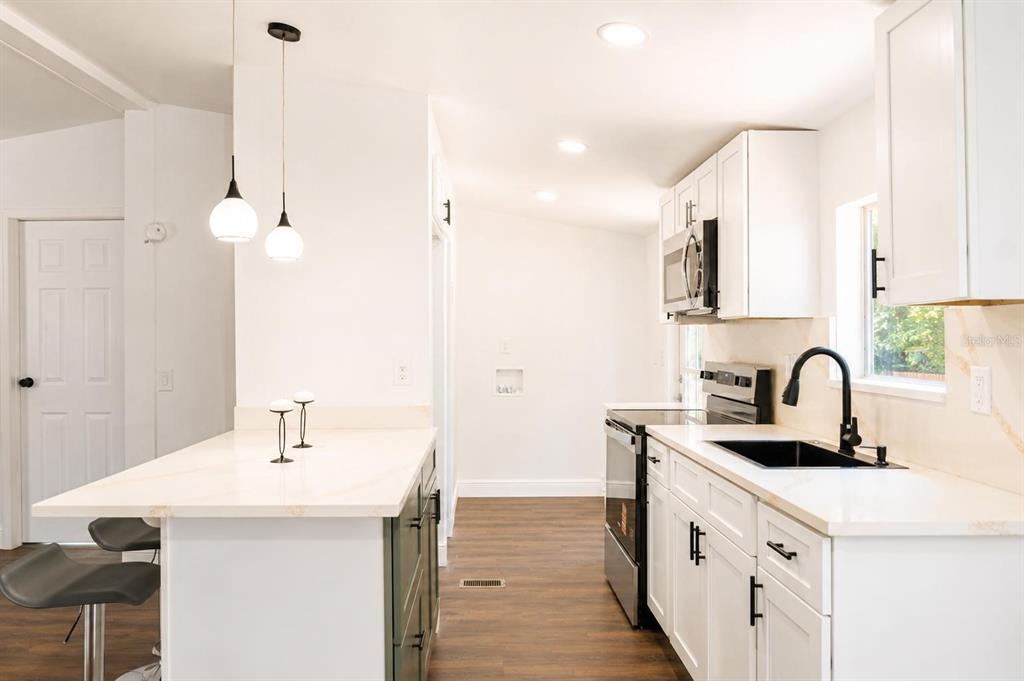 A modern kitchen features white cabinets, a white island, dark countertops, and wood-look flooring — 1809 NE 162ND STREET, CITRA, FL