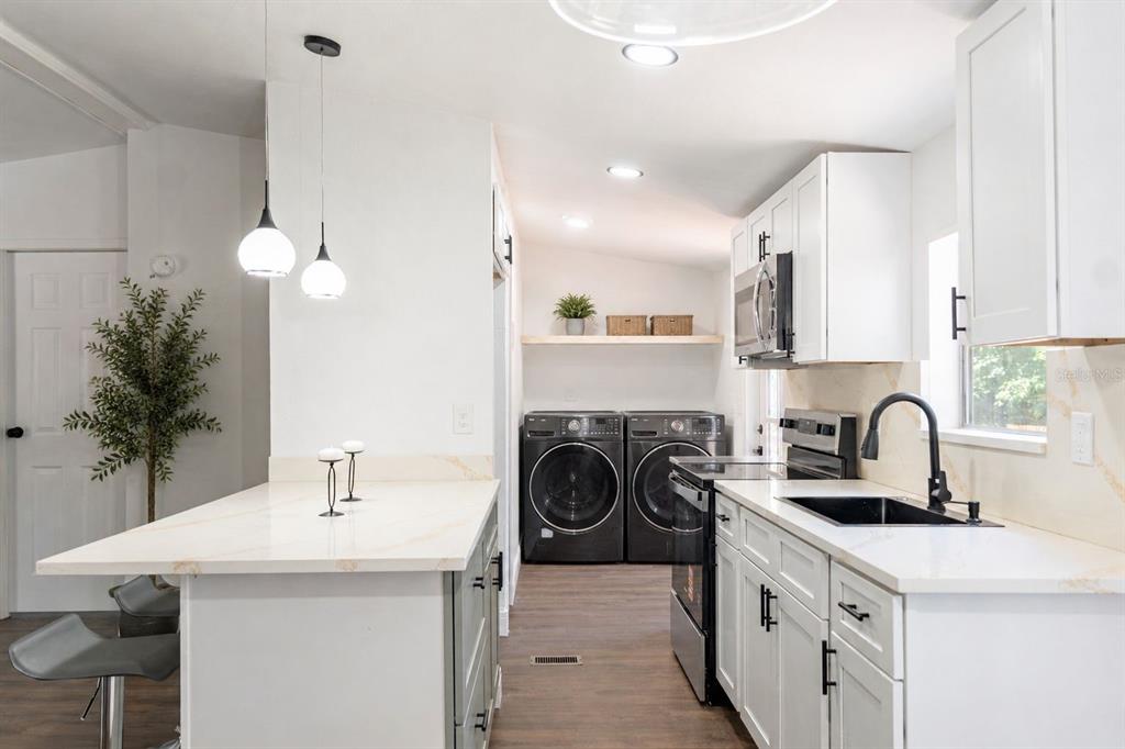 A kitchen with white cabinets, quartz countertops, a black sink, and an adjacent laundry area — 1809 NE 162ND STREET, CITRA, FL