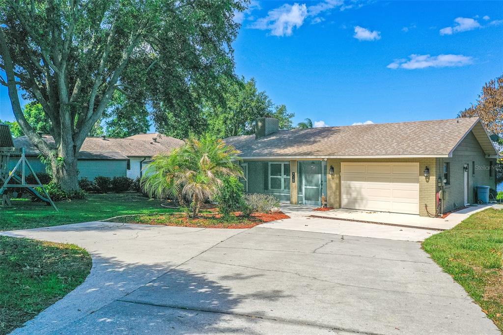 A single-story brick house with a garage, a concrete driveway, and a large front tree — 715 S LAKESIDE TERRACE, EAGLE LAKE, FL