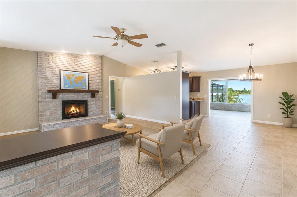A living room features a brick fireplace, tile flooring, and a view of a lake — 715 S LAKESIDE TERRACE, EAGLE LAKE, FL