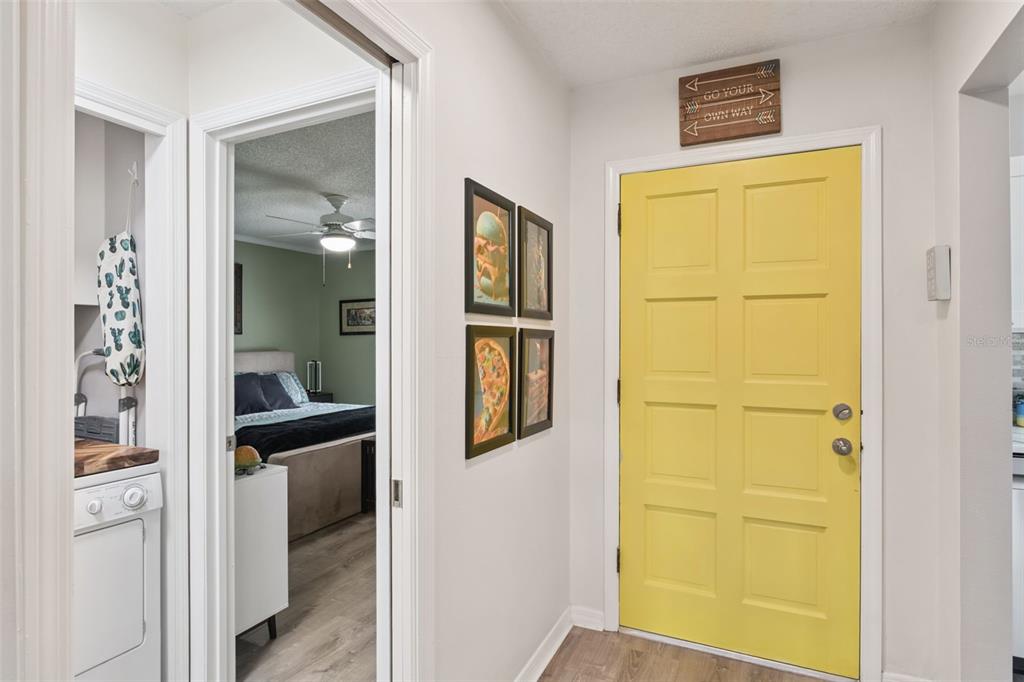 A hallway features a bright yellow door, framed wall art, and a view into a bedroom — 1112 VILLA LANE UNIT 84, APOPKA, FL