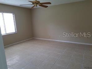 An empty room with beige walls, a ceiling fan, and light-colored tile flooring — 2 PERTHSHIRE LANE, PALM COAST, FL
