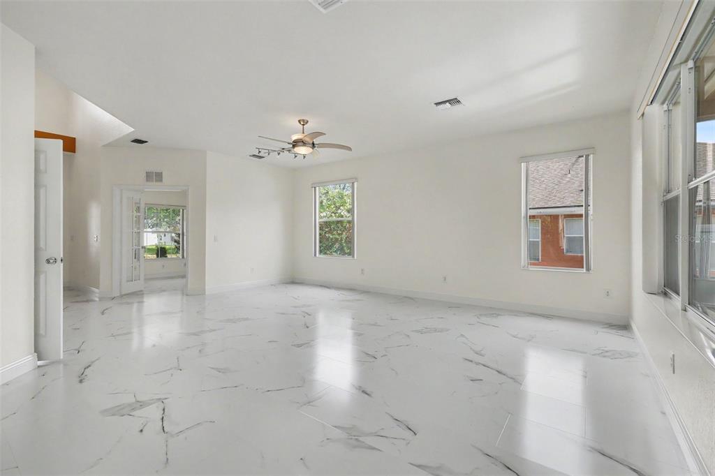 A bright, empty room features white marble-look tile flooring, white walls, and a ceiling fan — 4014 SW 51ST COURT, OCALA, FL