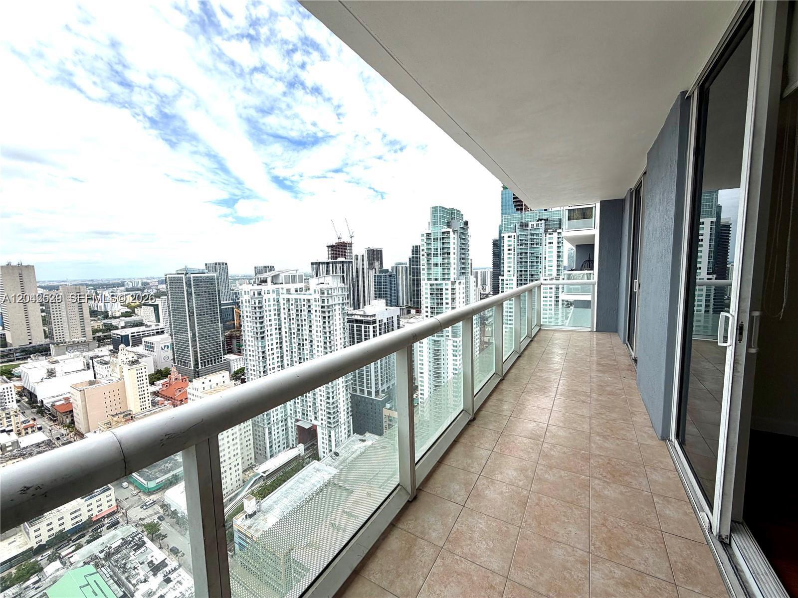 A high-rise balcony with tiled flooring overlooks a dense city skyline under a cloudy sky — 50 Biscayne Blvd # 4507, Miami FL 33132, MIAMI, FL