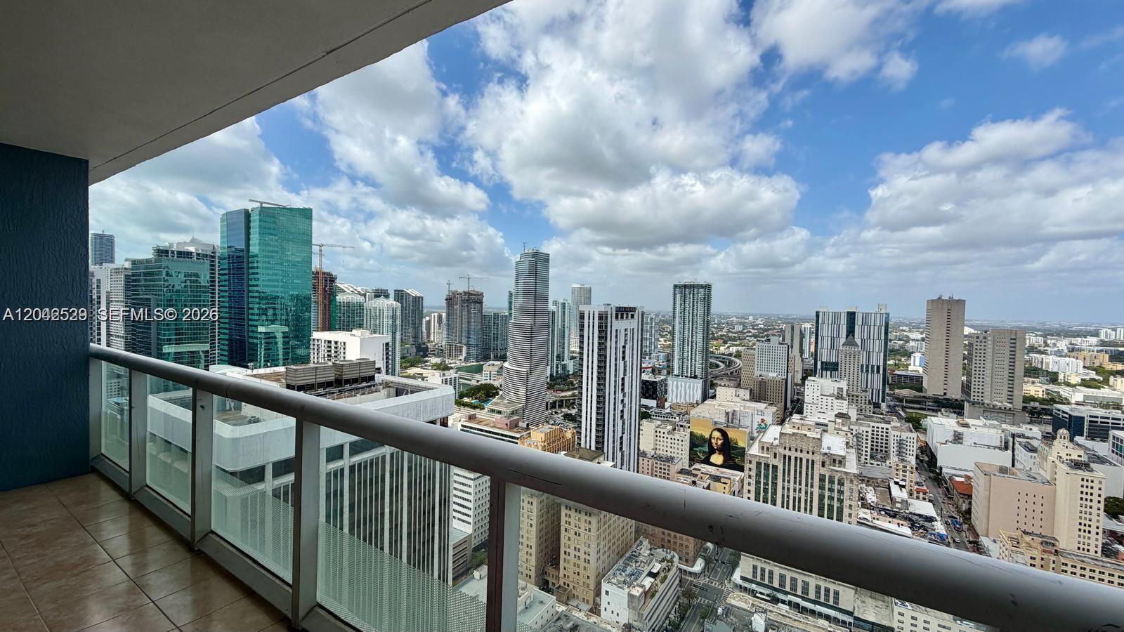 A high-rise balcony overlooks a dense urban skyline under a cloudy blue sky — 50 Biscayne Blvd # 4507, Miami FL 33132, MIAMI, FL