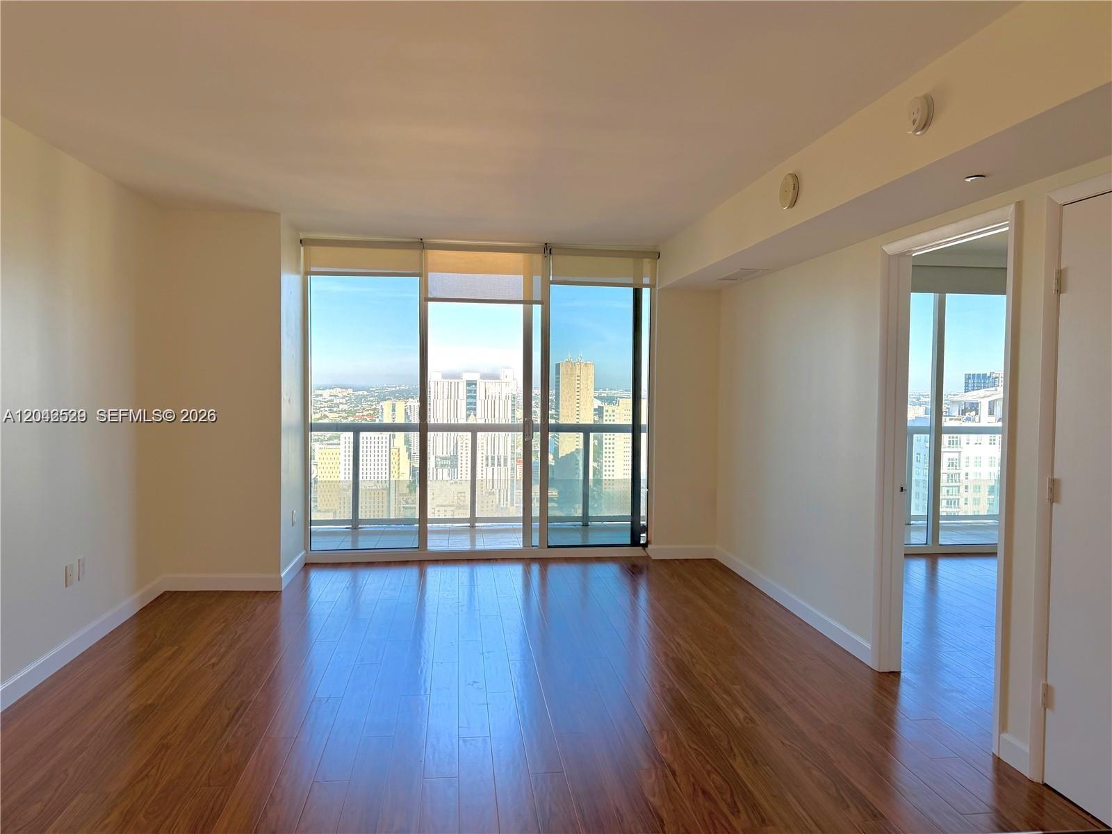 An empty room with hardwood floors, floor-to-ceiling windows, and a balcony overlooking a city skyline — 50 Biscayne Blvd # 4507, Miami FL 33132, MIAMI, FL