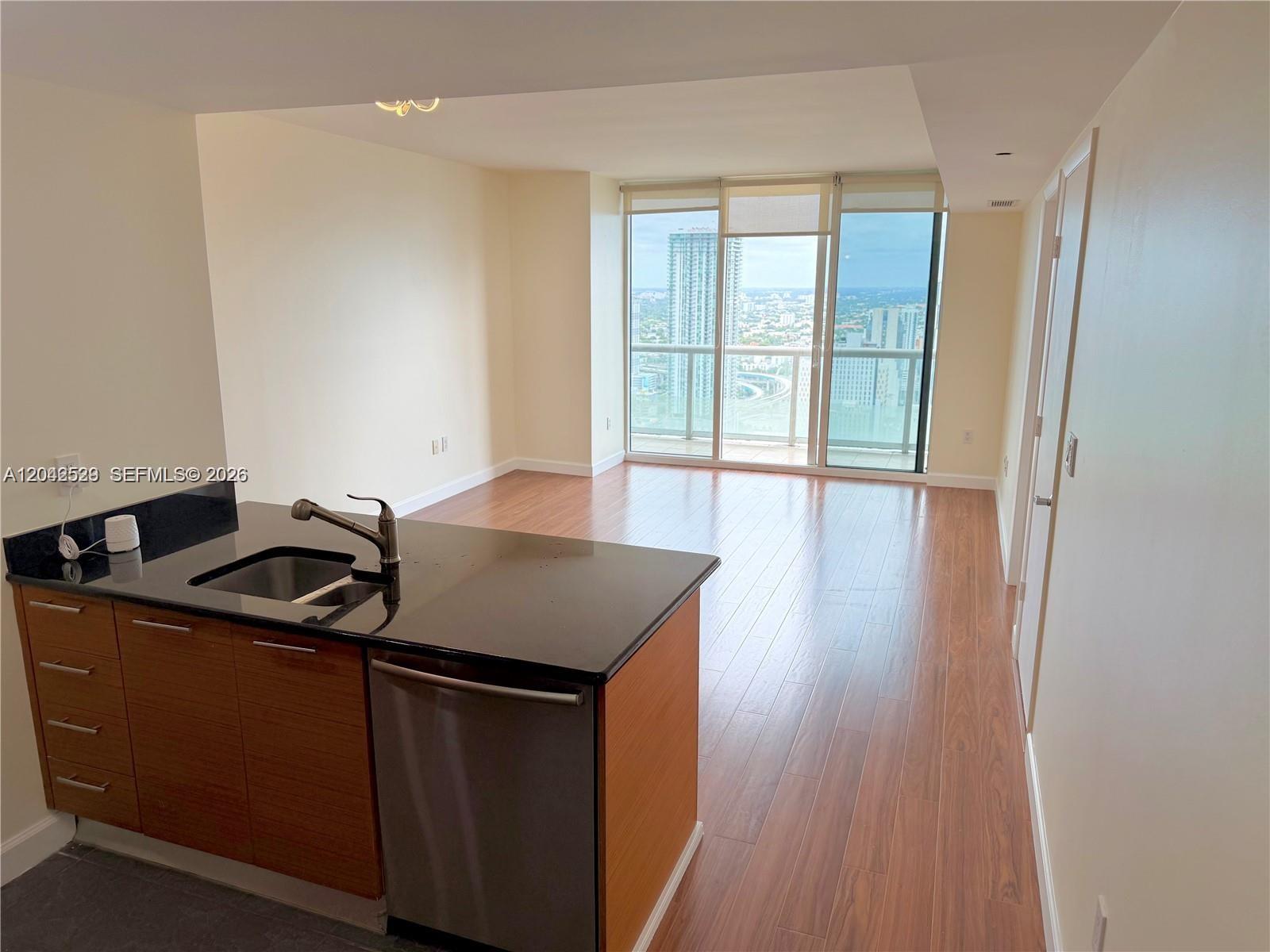 A kitchen island with a black countertop overlooks an empty living area with floor-to-ceiling windows — 50 Biscayne Blvd # 4507, Miami FL 33132, MIAMI, FL