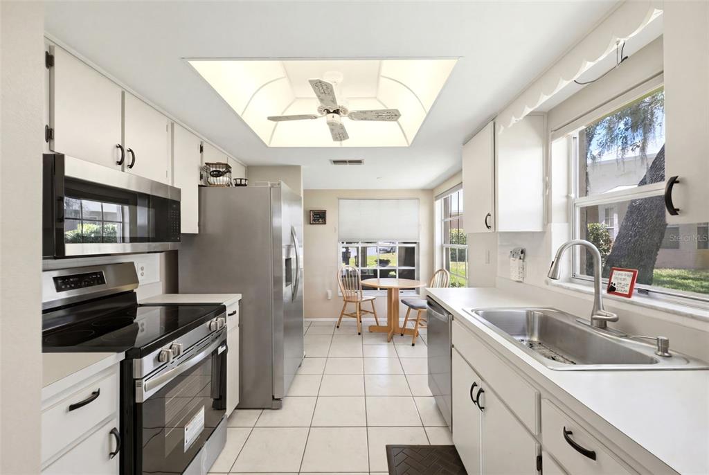 A kitchen with white cabinets, stainless steel appliances, tile flooring, and a small dining area — 4903 LEYTE COURT UNIT 67, NEW PORT RICHEY, FL
