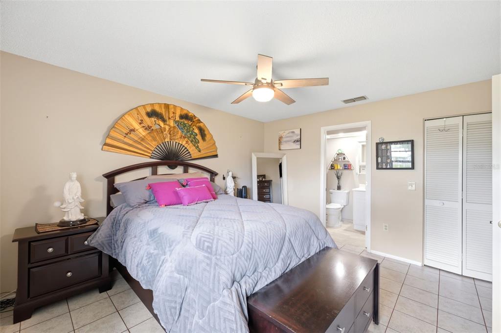 A bedroom features a bed with a large decorative fan, tile flooring, and an attached bathroom — 4903 LEYTE COURT UNIT 67, NEW PORT RICHEY, FL