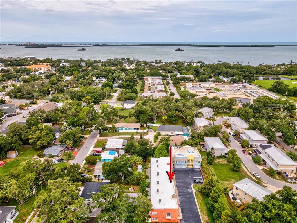 An aerial view shows a multi-story building with a red arrow pointing to its roof — 553 LUSARA COURT, DUNEDIN, FL