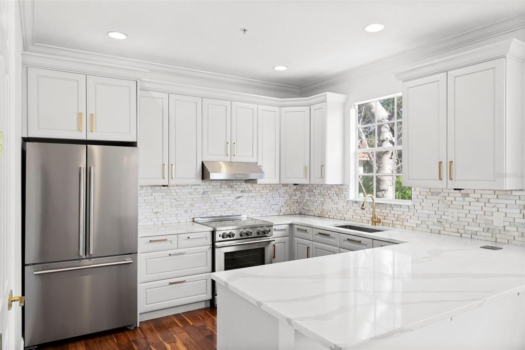 A kitchen with white cabinets, stainless steel appliances, marble backsplash, and a white quartz countertop — 2605 ESPANA COURT, TAMPA, FL