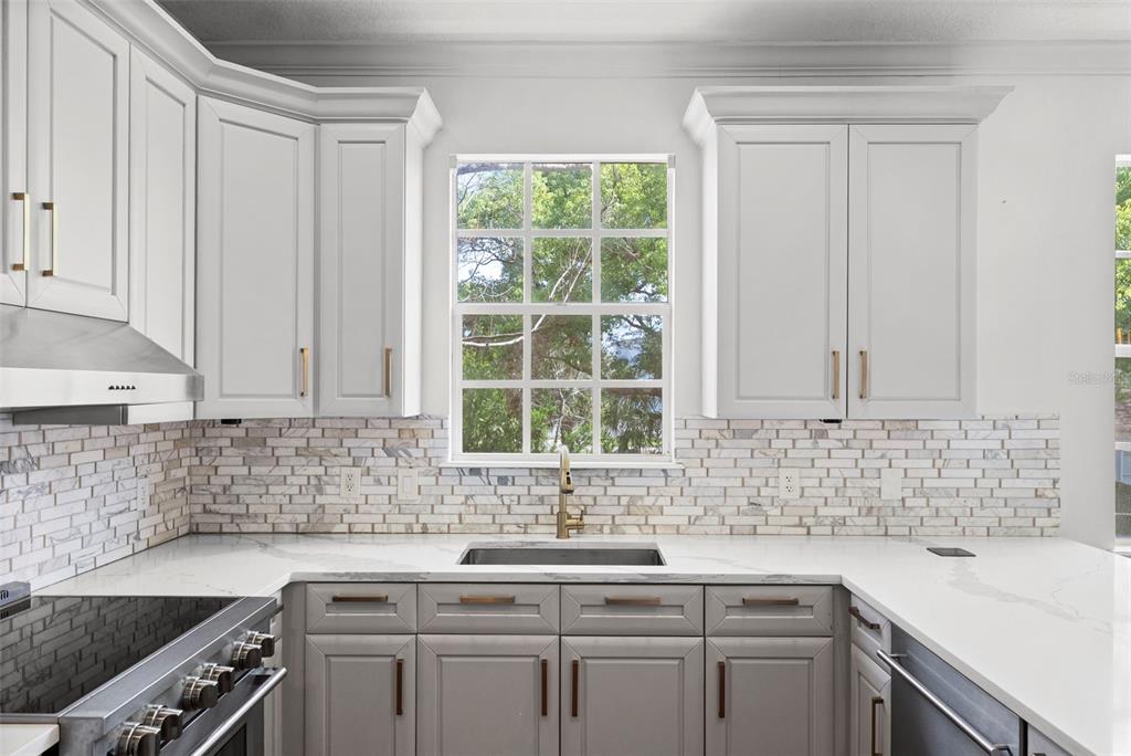 A kitchen features white upper cabinets, gray lower cabinets, marble tile backsplash, and a window — 2605 ESPANA COURT, TAMPA, FL