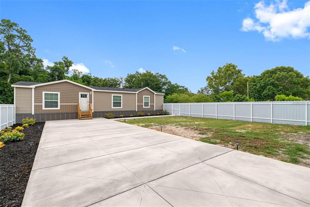 A manufactured home with tan siding sits behind a large concrete driveway and fence — 17151 LEMON STREET, SPRING HILL, FL