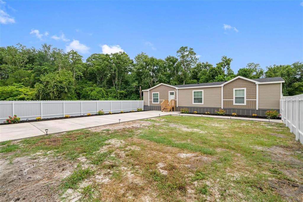 A manufactured home with a concrete driveway and white vinyl fence sits on a lot — 17151 LEMON STREET, SPRING HILL, FL