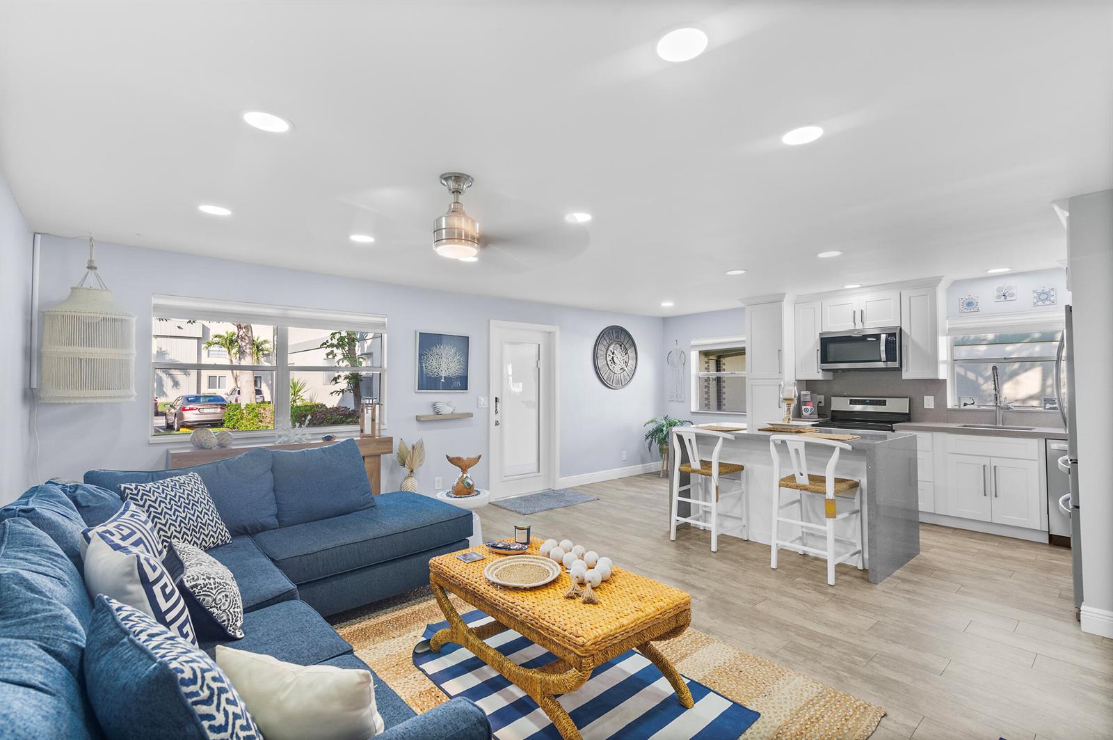 An open-concept living room and kitchen feature a blue sectional, wicker coffee table, and island — 244 Monaco F, Delray Beach FL 33446, DELRAY BEACH, FL