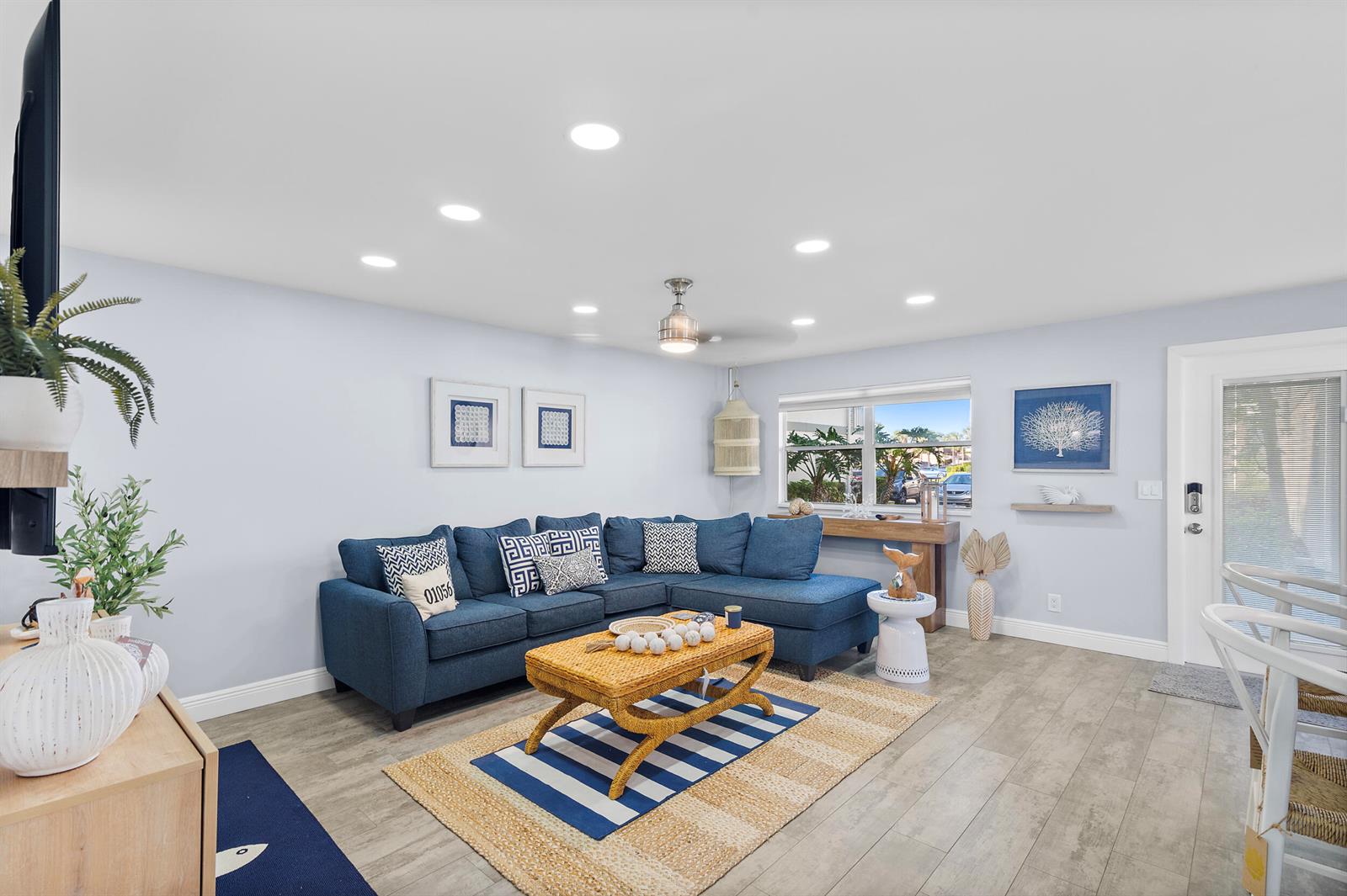 A living room features a blue sectional sofa, a wicker coffee table, and light flooring — 244 Monaco F, Delray Beach FL 33446, DELRAY BEACH, FL