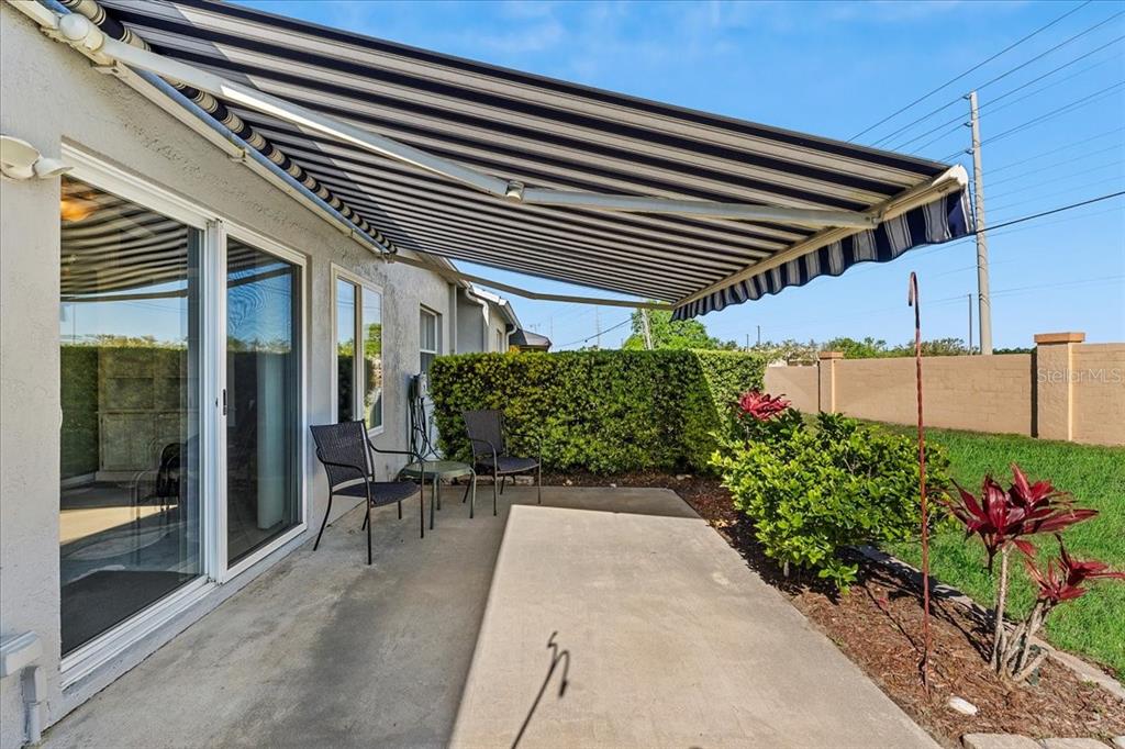 A concrete patio features a retractable striped awning, two chairs, and a small table — 6381 EGRET DRIVE UNIT 19, LAKELAND, FL