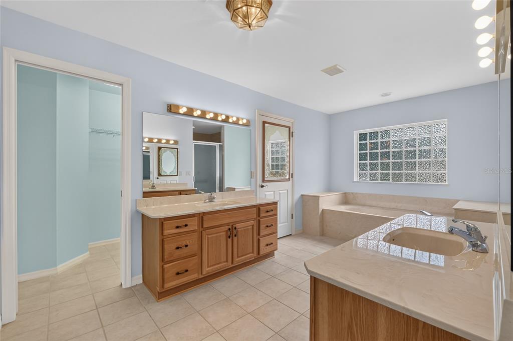 A bathroom features a double vanity with wood cabinets, a soaking tub, and glass block windows — 4647 NE 15TH STREET, OCALA, FL