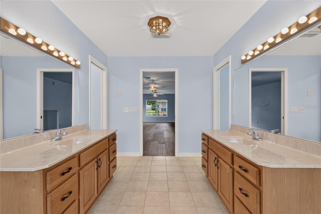A bathroom features dual wooden vanities with marble countertops, large mirrors, and light blue walls — 4647 NE 15TH STREET, OCALA, FL