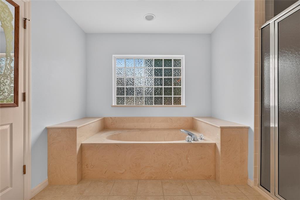 A bathroom features a beige stone-tiled soaking tub beneath a glass block window — 4647 NE 15TH STREET, OCALA, FL