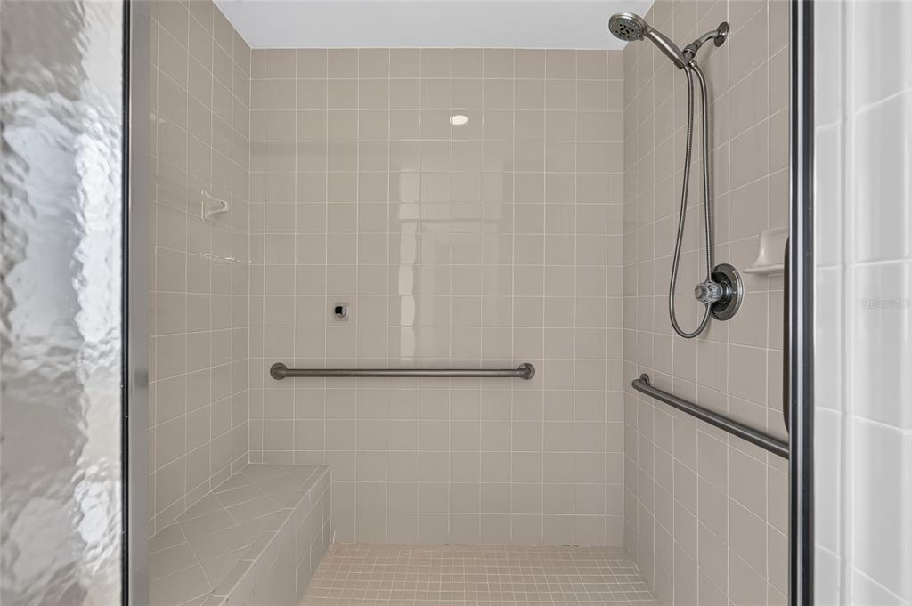 A tiled walk-in shower features a built-in bench, two grab bars, and a handheld showerhead — 4647 NE 15TH STREET, OCALA, FL