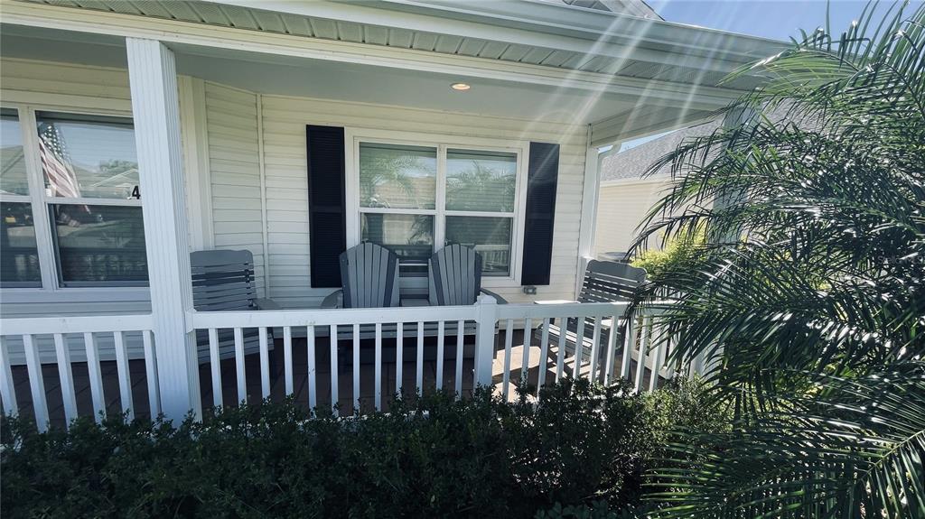 A covered front porch features white railings, three gray Adirondack chairs, and black window shutters — 443 POMEGRANATE PATH, THE VILLAGES, FL