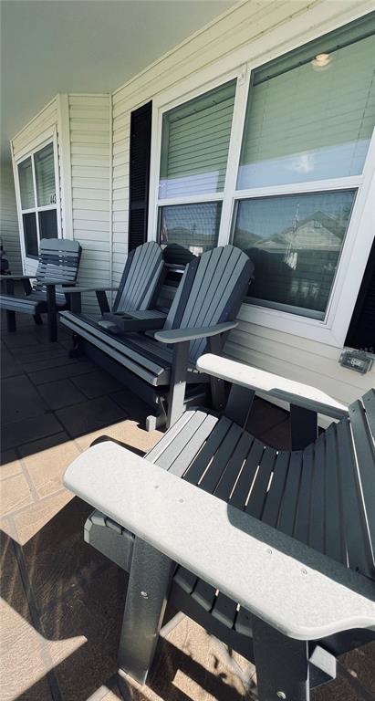 A covered porch features several gray Adirondack-style chairs and a bench with a center console — 443 POMEGRANATE PATH, THE VILLAGES, FL