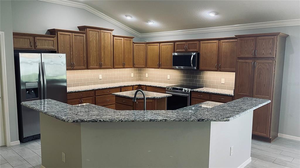 A kitchen features wood cabinets, granite countertops, stainless steel appliances, and a central island — 443 POMEGRANATE PATH, THE VILLAGES, FL