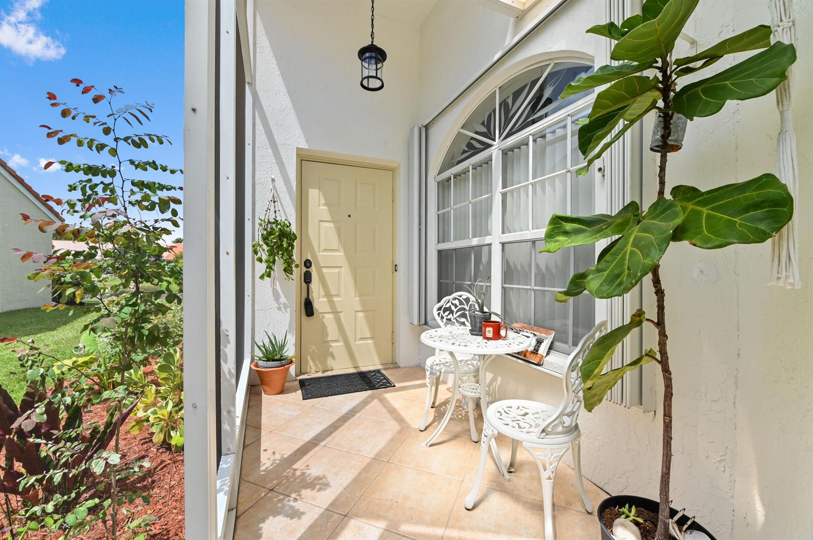 A covered patio features a small bistro set, a potted plant, and a front door — 6077 Lake Hibiscus Drive, Delray Beach FL 33484, DELRAY BEACH, FL