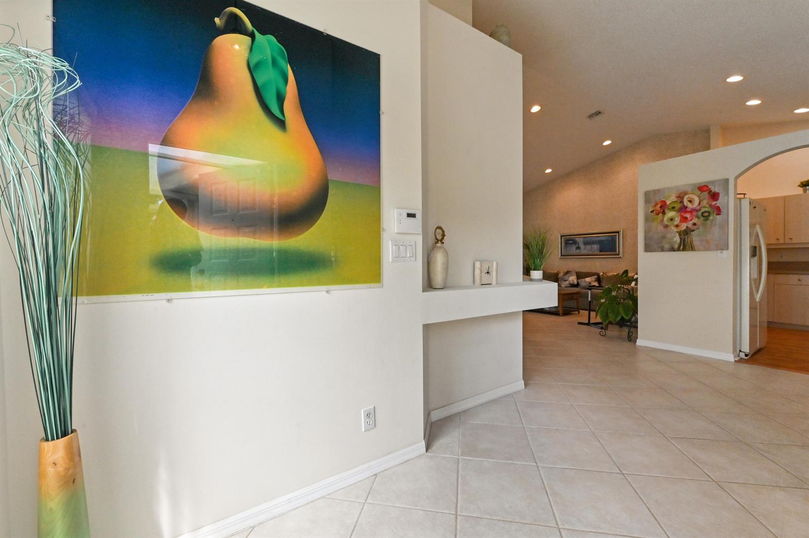 A bright entryway features a large pear print, a built-in shelf, and tiled flooring — 6077 Lake Hibiscus Drive, Delray Beach FL 33484, DELRAY BEACH, FL
