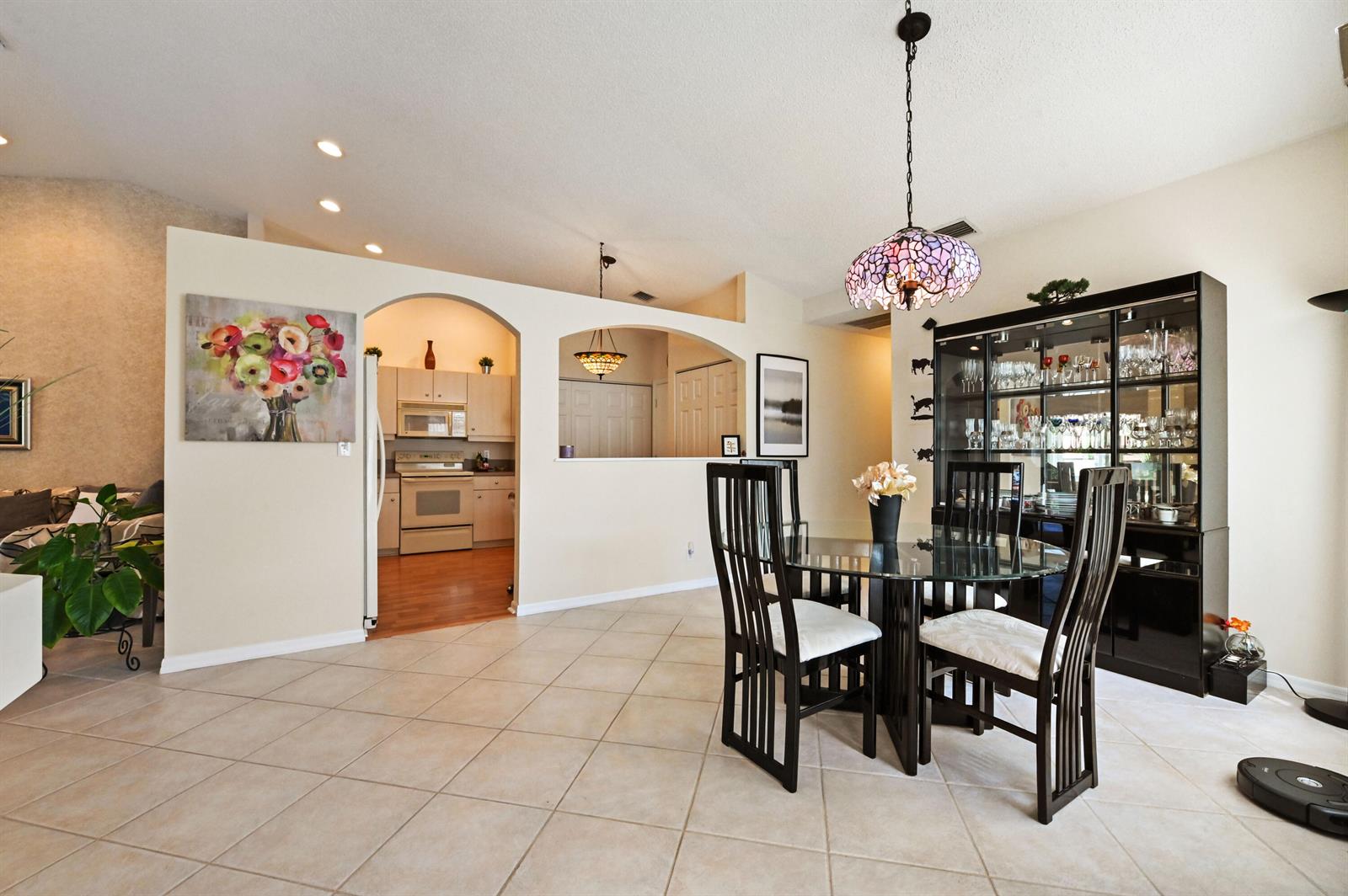 A dining area with a glass table and hutch opens to a kitchen with arches — 6077 Lake Hibiscus Drive, Delray Beach FL 33484, DELRAY BEACH, FL